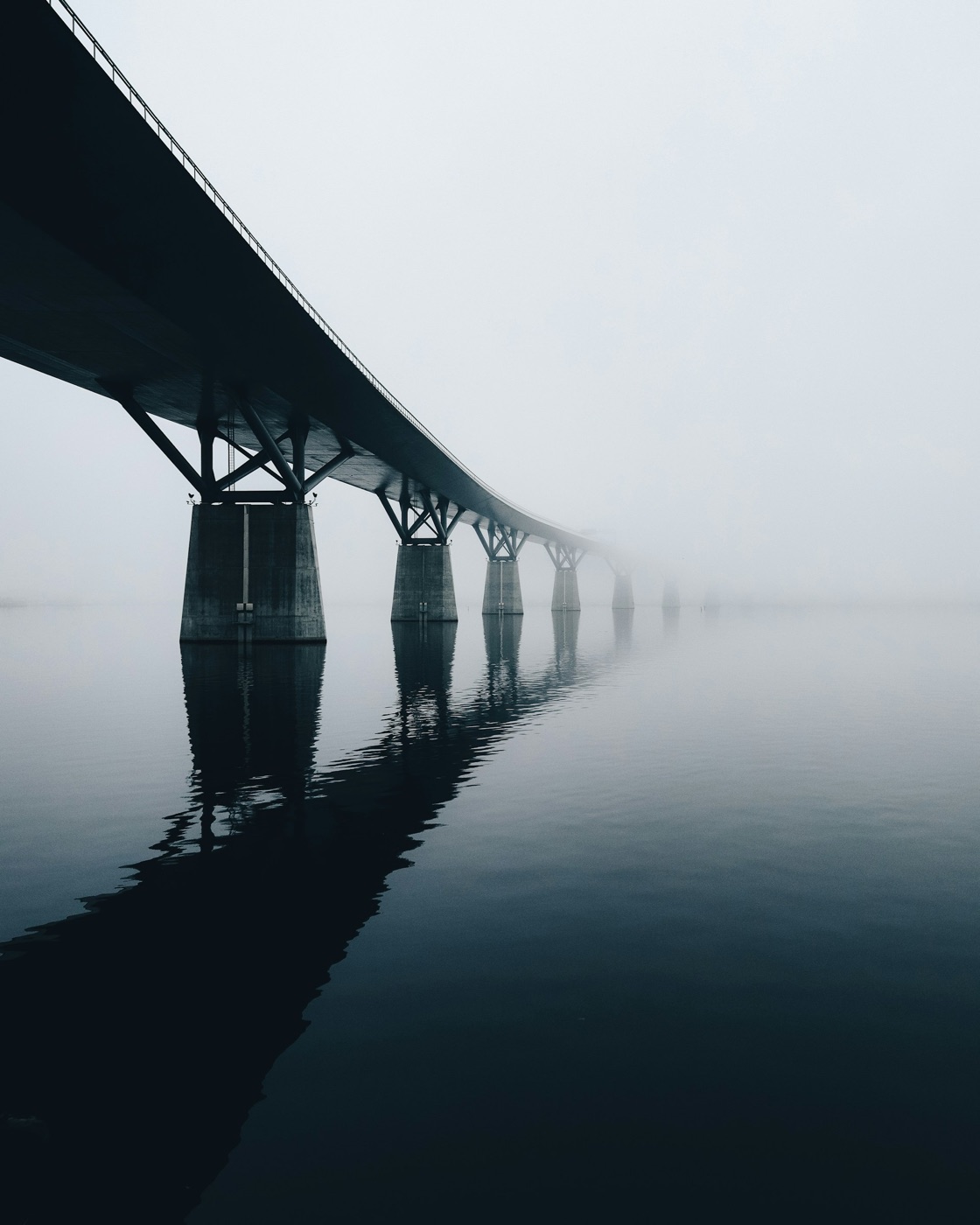 A long bridge fades into mist over still water