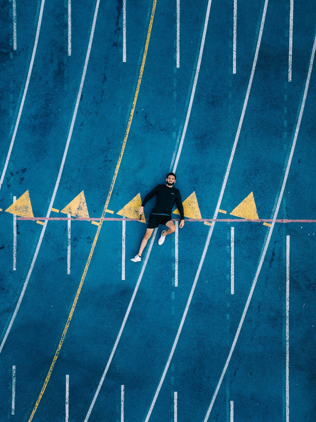 Aerial view of a runner lying at the starting line of a blue track